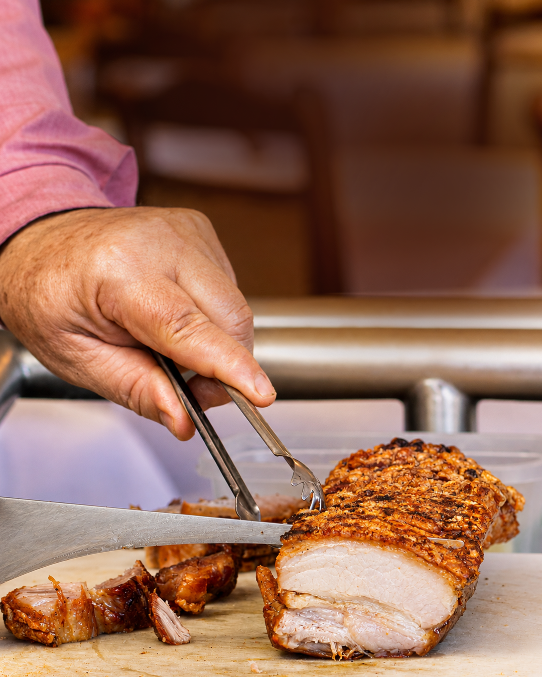 Mãos fatiando carne assada com faca e pinça