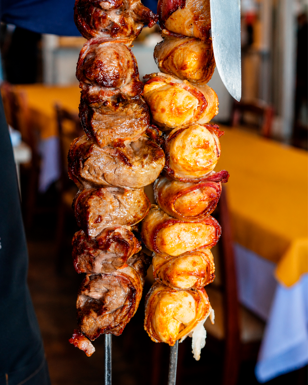 Espetos de carne dourada sendo finalizados com uma faca